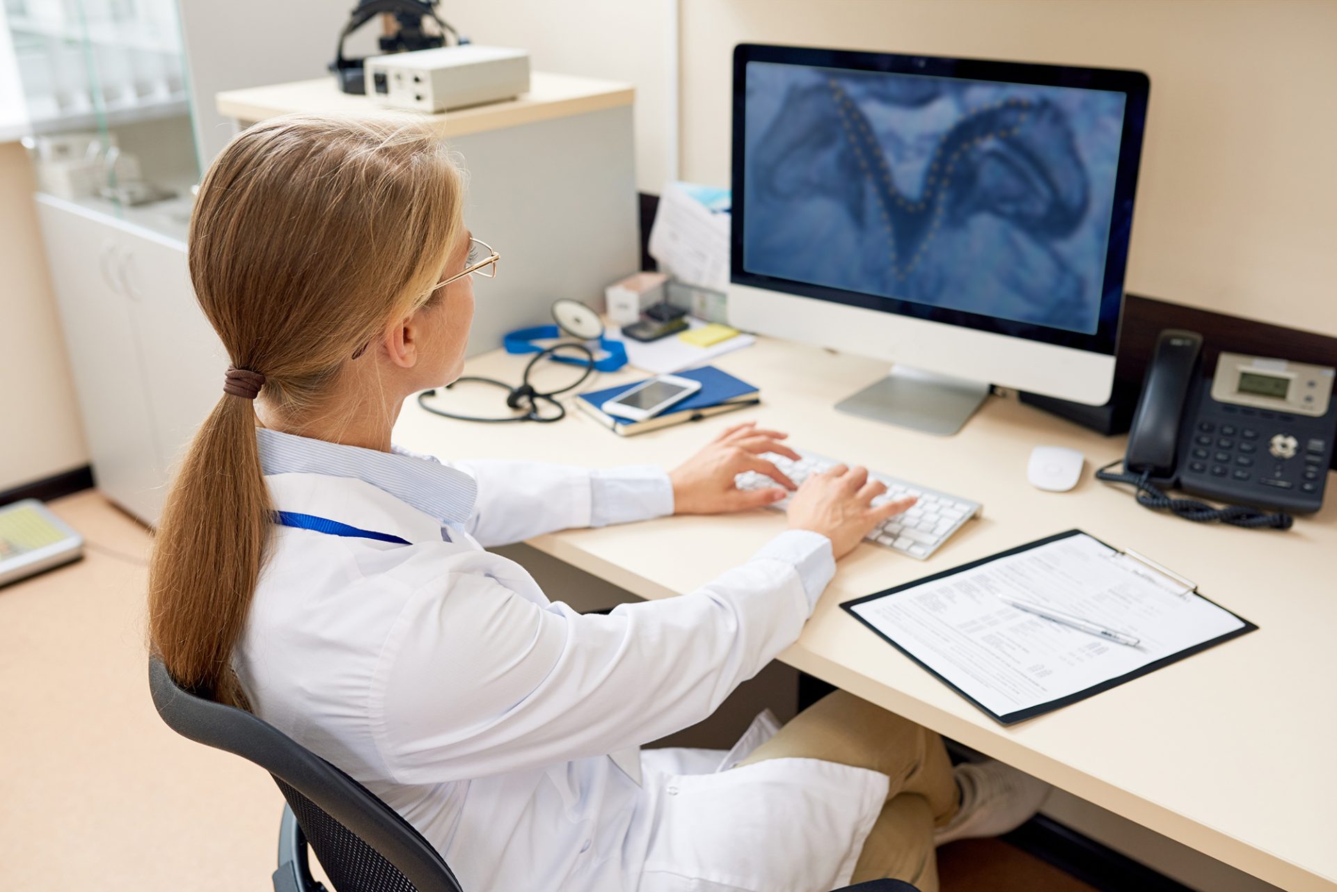 Back view of a female doctor looking at an MRI of lumbar spinal stenosis on screen